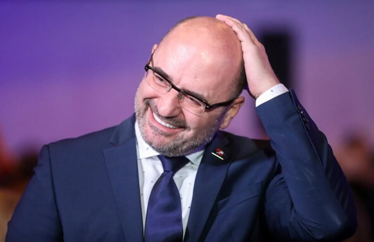 Portret nasmijanog Milijana Brkića u tamnom odijelu i naočalama