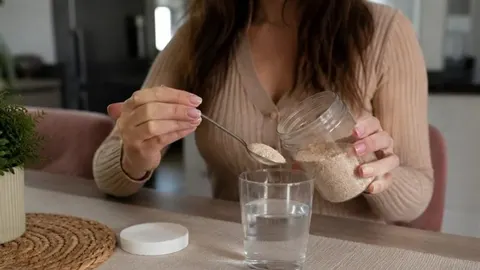 Žena s žlicom ljuskica psilijuma iznad čaše vode