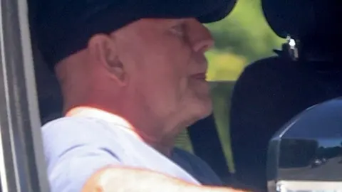 Profil glumeča Brucea Willisa u automobilu koji nosi crni šešir