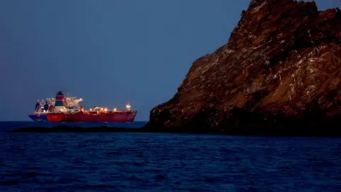 Veliki crveni tanker za naftu plovi oceanom pored stjenovite obale