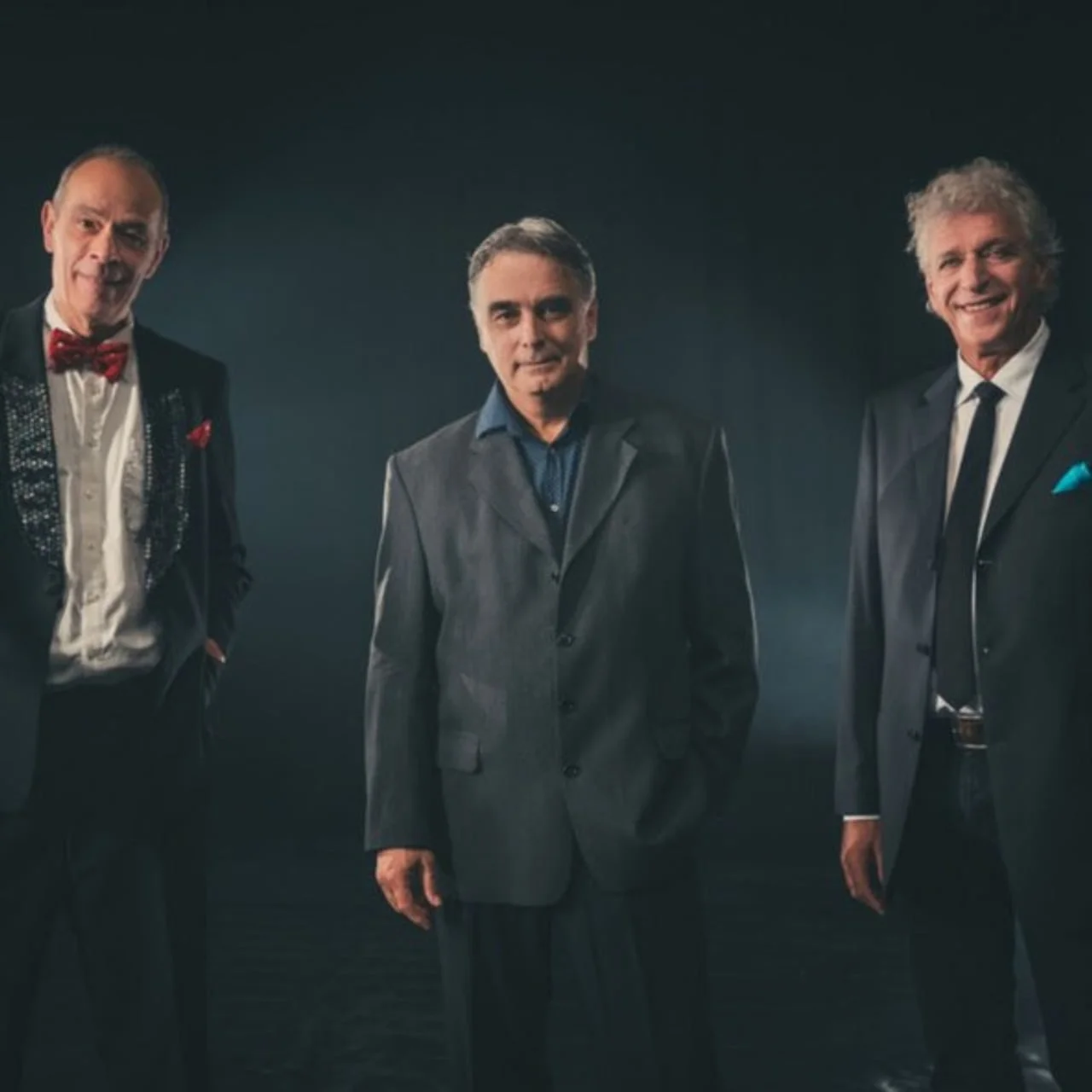 Tri muškarca u elegantnim odijelima pred tamnom pozadinom