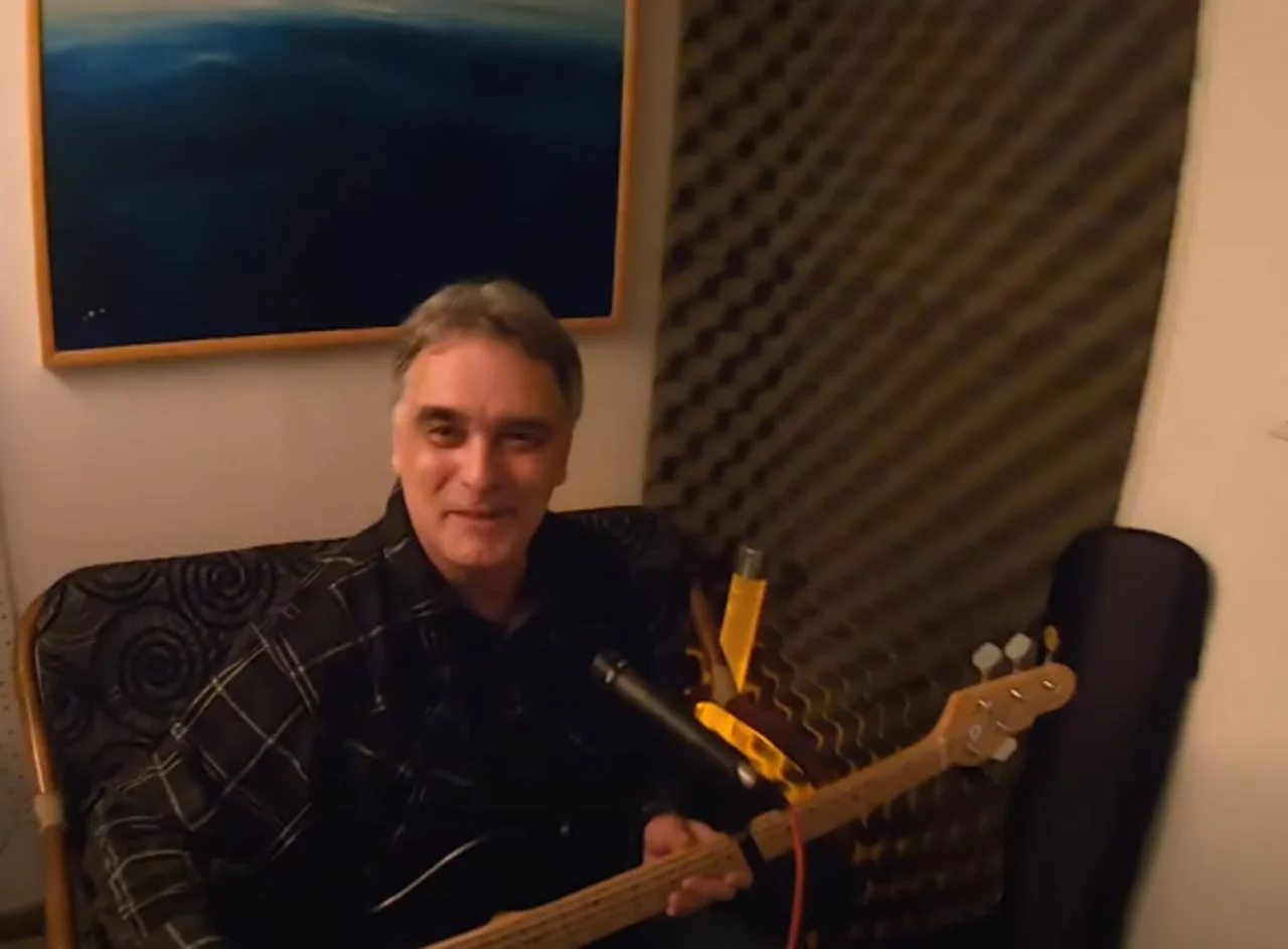Muškarac u crnoj košulji s električnom gitarom u zatvorenom prostoru