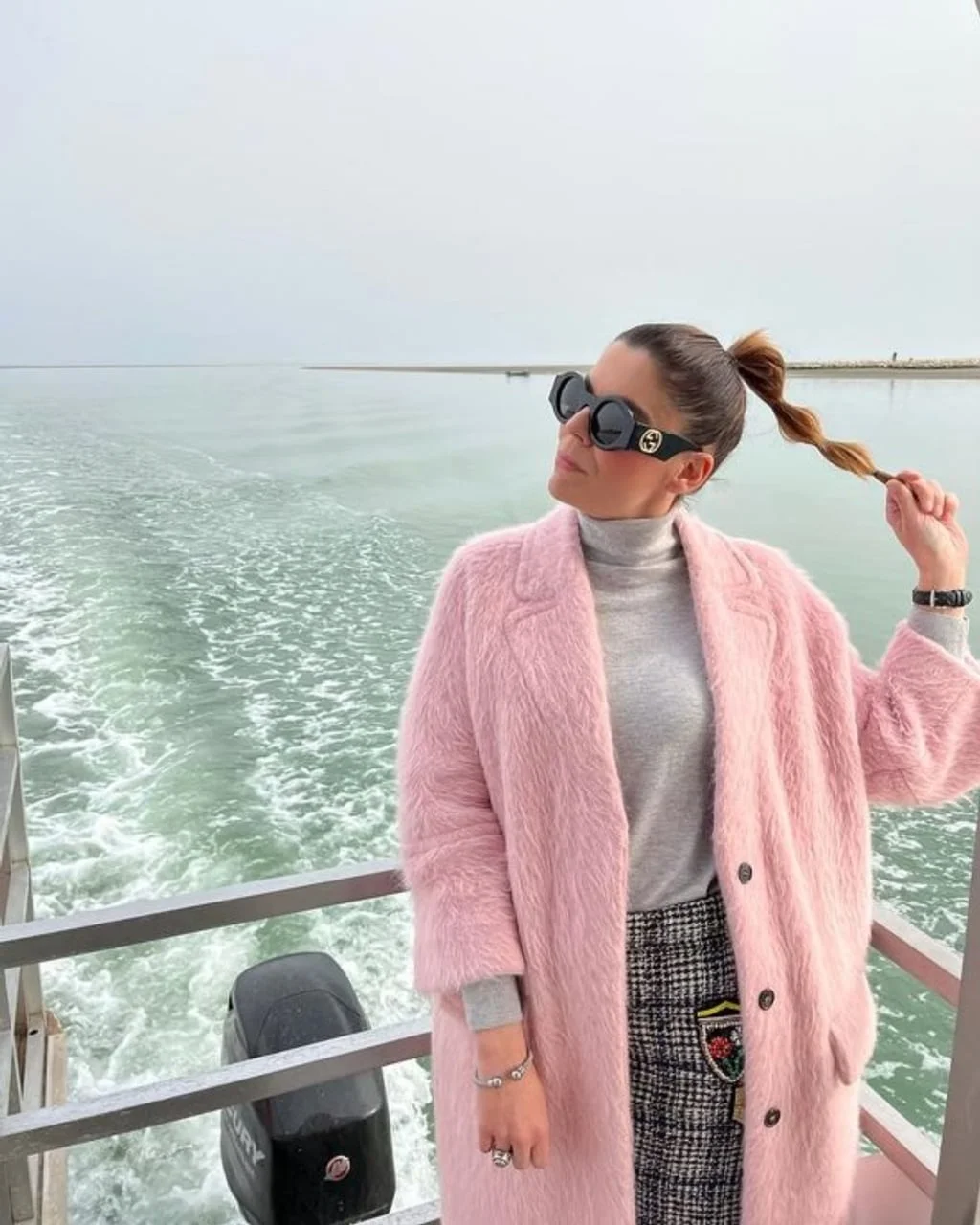 Žena u ružičastom kaputu i sunčanim naočalama na brodu
