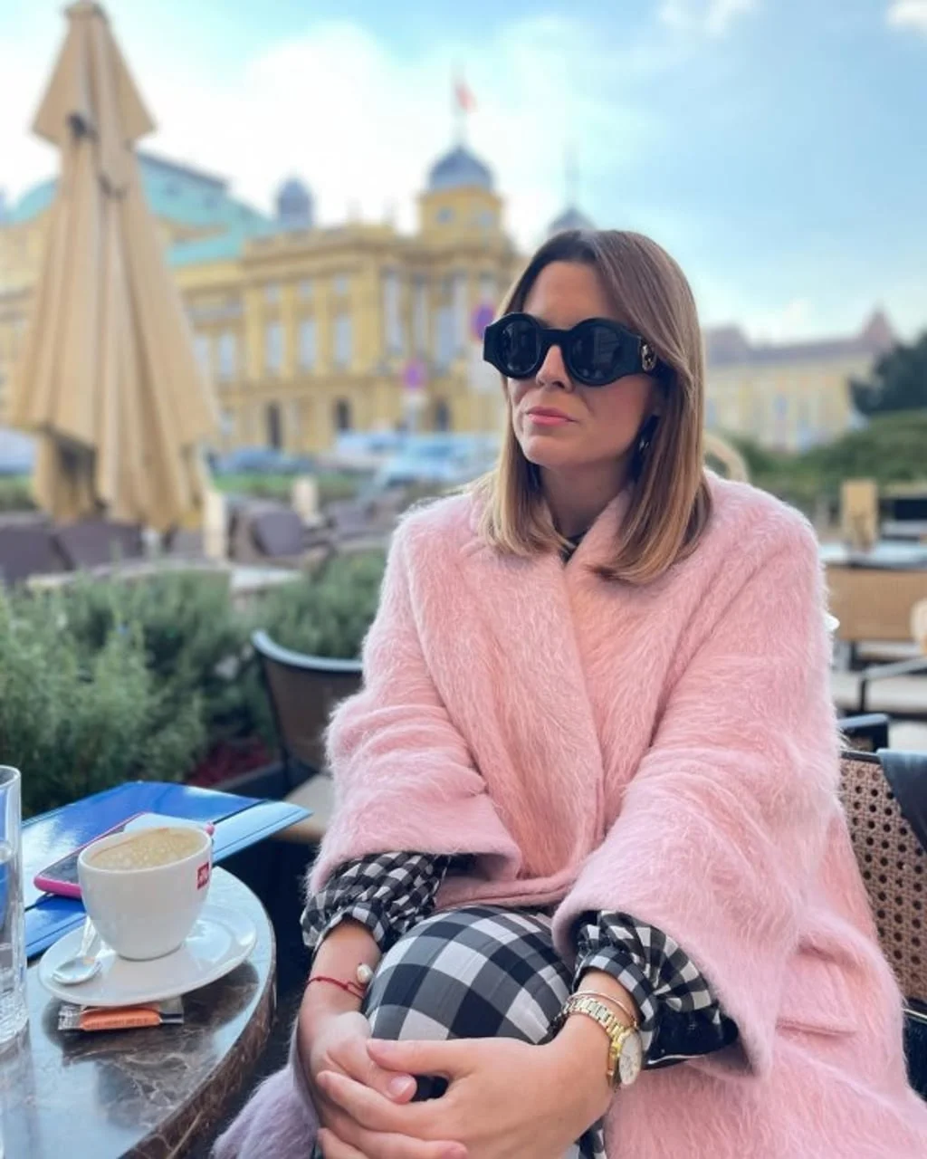 Žena u ružičastom kaputu s kavom na terasi u gradu