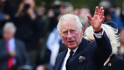 Kralj Charles III u tamnom odelu maše rukom masi ljudi