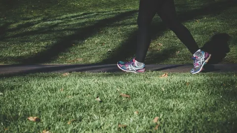 Osoba u sportskoj odjeći i tenisicama hoda stazom kroz zeleni park
