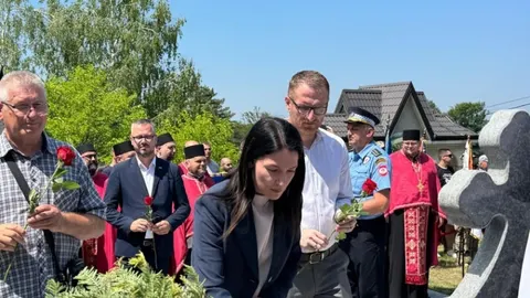 Grupa ljudi s crvenim ružama stoji ispred spomenika na otvorenom