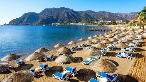 Pješčana plaža s redovima sunčanica i plavim ležaljkama uz more i planine