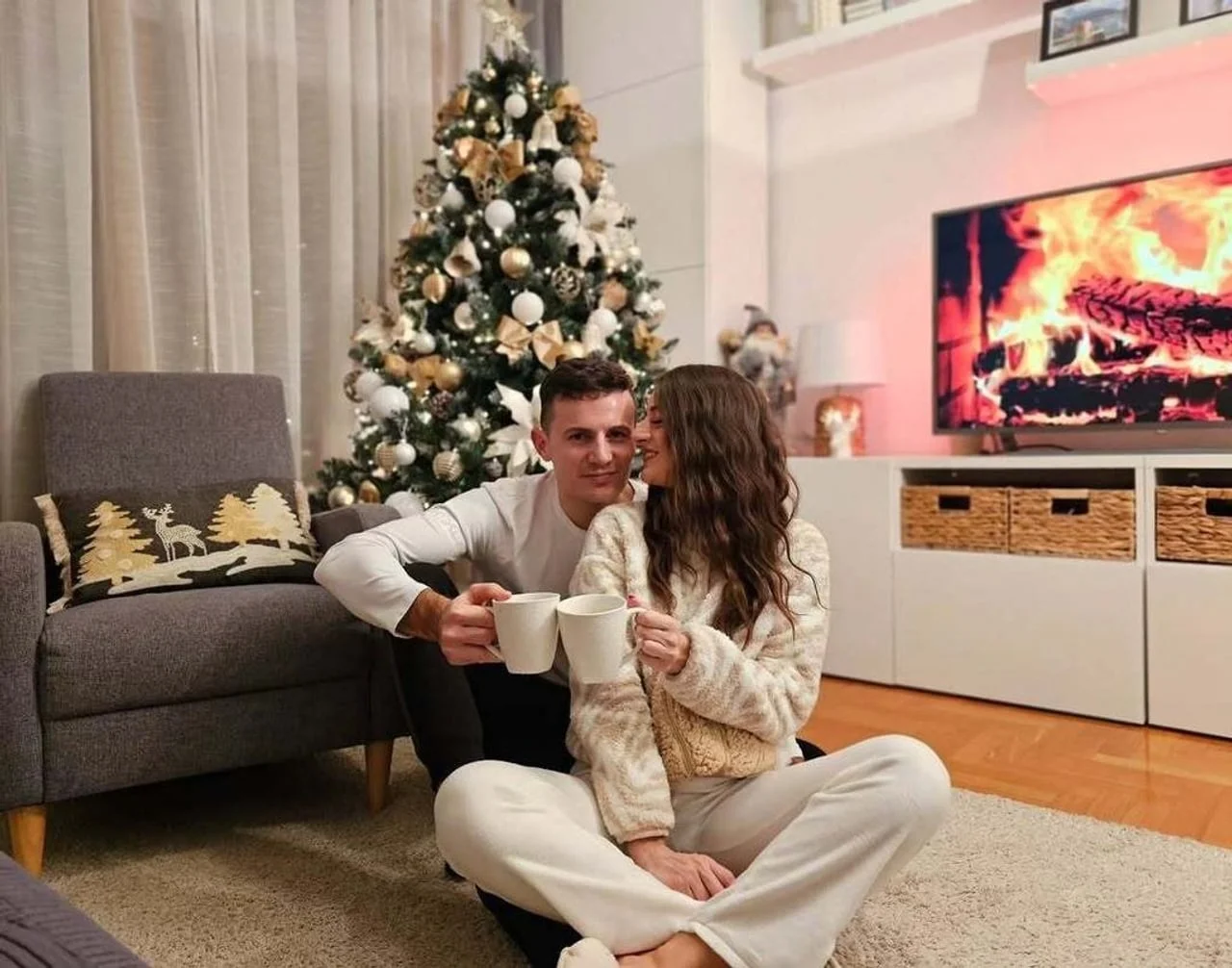Par s šalicama kave sjedi u dnevnom boravku pored ukrašenog bora