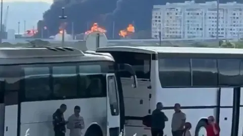 Veliki požar i crni dim u pozadini grada s bijelim zgradama i autobusima