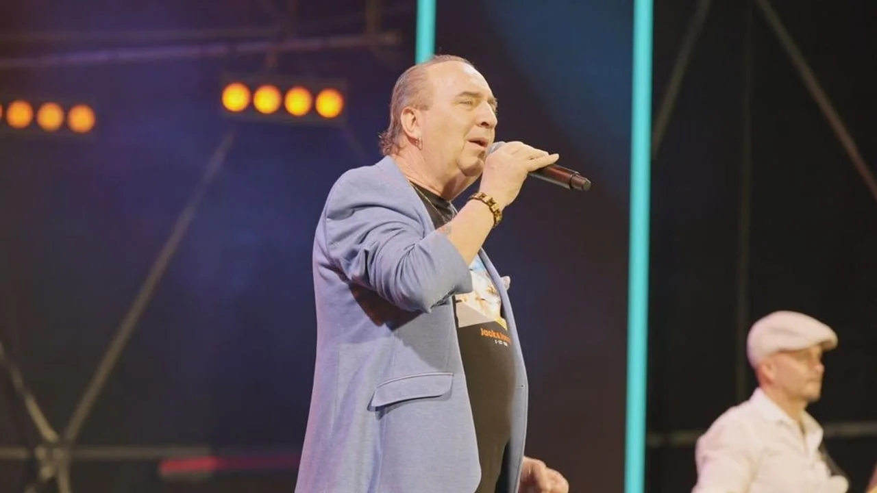 Mladen Grdović u plavom saku pjeva u mikrofon na koncertnoj pozornici