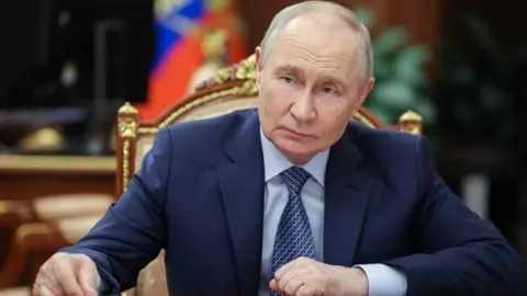 Vladimir Putin u tamnom odijelu sjedi u ukrasnom stolcu