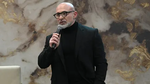 Miroslav Levak u crnom odelu drži mikrofon ispred mramornog zida