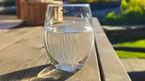 Čaša čiste vode na drvenom stolu na suncu