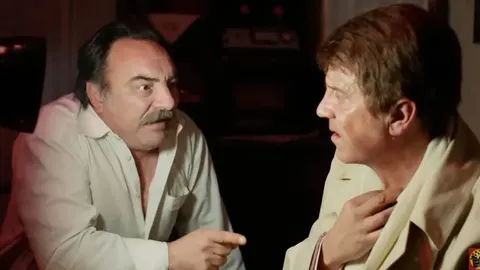 Dva muškarca u napetom razgovoru, jedan s brkovima u bijeloj košulji