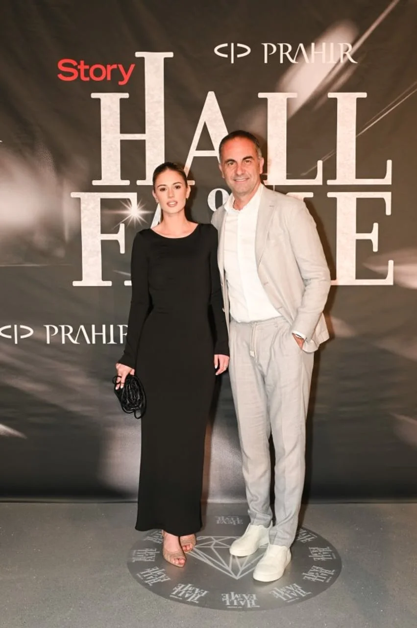Žena u crnoj haljini i muškarac u svijetlom odelu ispred zida