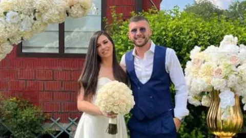 Ante Rebić u plavom odijelu stoji pored brinete u bijeloj haljini s buketom cvijeća.