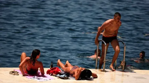 Ljudi sunčaju se i kupaju na sunčanim stijenama pored plavog mora