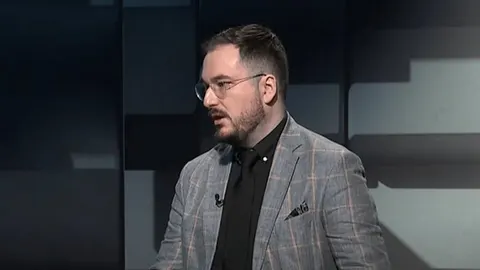 Muškarac s naočalama i bradom u sivom sako i crnoj košulji