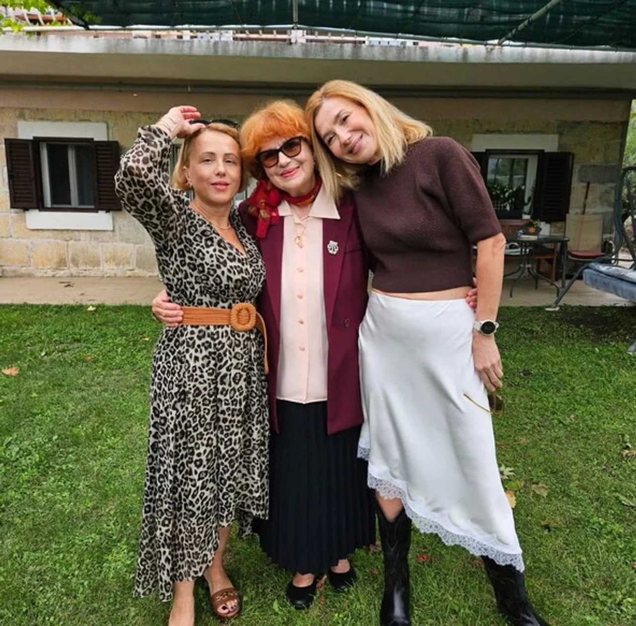 Tri žene stoje u vrtu odjevene u modnu odjeću