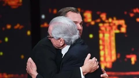 Dva muškarca u crnim odelima grle se na sceni