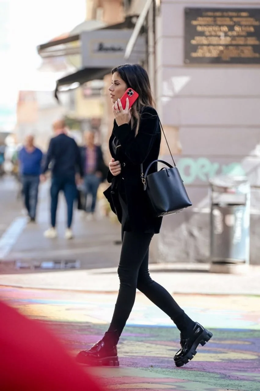 Žena u crnim hlačama i saku razgovara telefonom u hodu