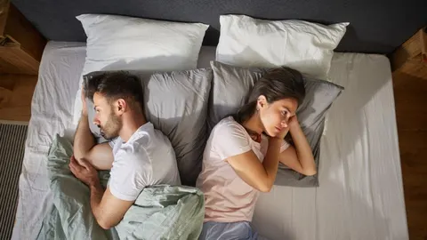 Muškarac i žena leže u krevetu okrenuti leđima jedan drugom