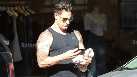 Joe Manganiello u crnom tank topu s tetovažiranim rukama gleda u mobitel