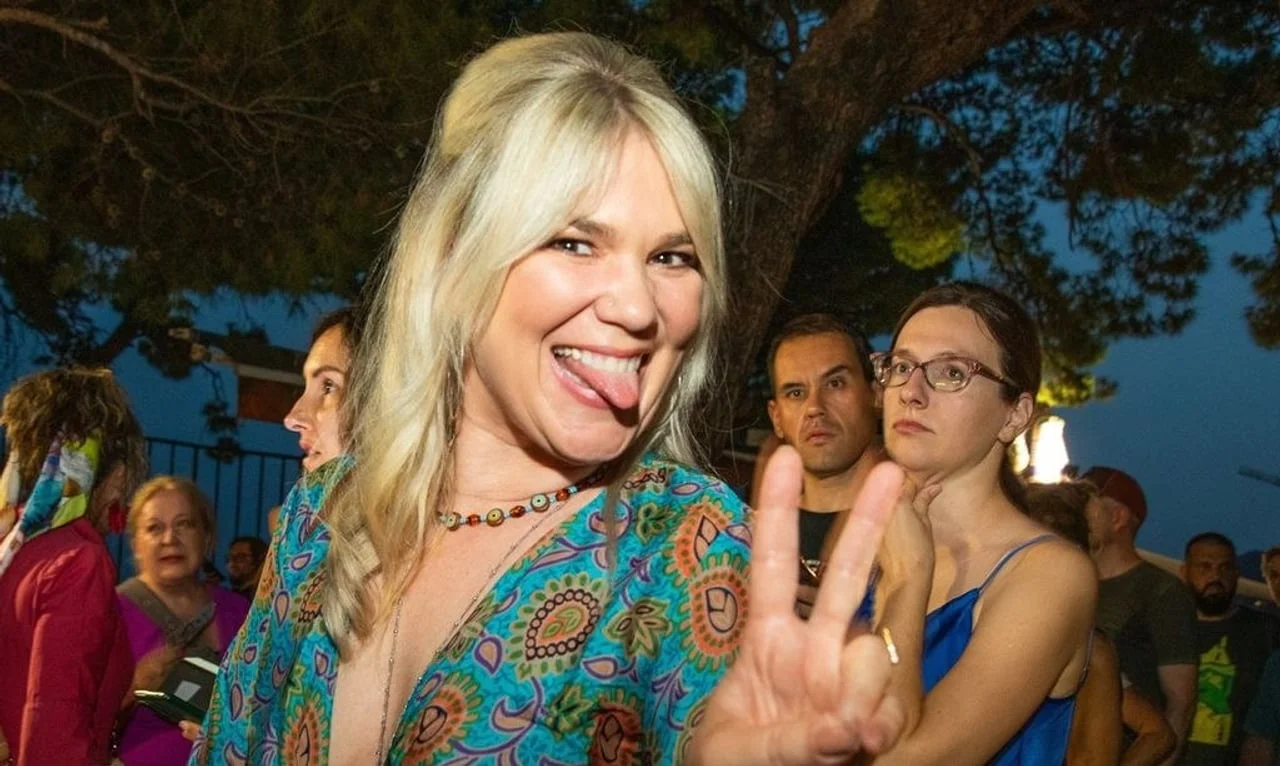 Plavuša u šarenoj haljini koja pokazuje znak mira i smije se