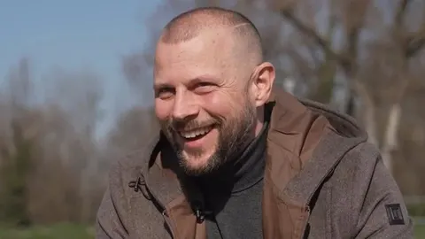 Portret nasmijanog Alana Hržice u smeđoj jakni na otvorenom
