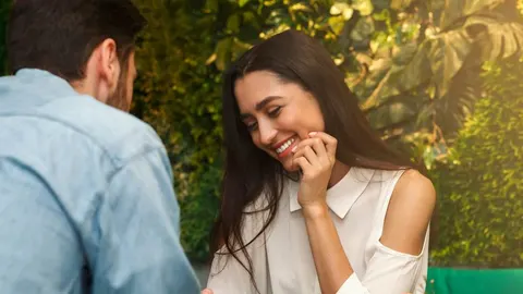 Osmijana žena u bijeloj bluzi razgovara s muškarcem u parku