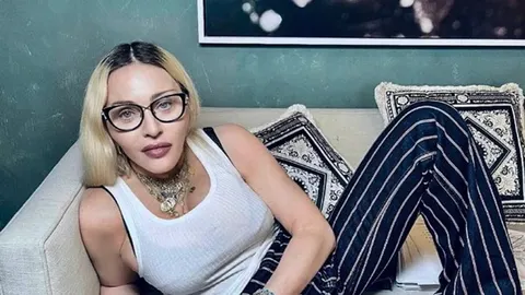 Madona s naočalama za vid i nakitom opušteno leži na svijetlom kauču