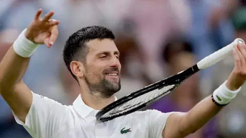 Novak Đoković u bijeloj polo majici drži teniski reket i smije se