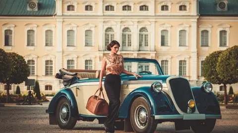 Elegantna žena s kožnom torbom pored plavog vintage automobila