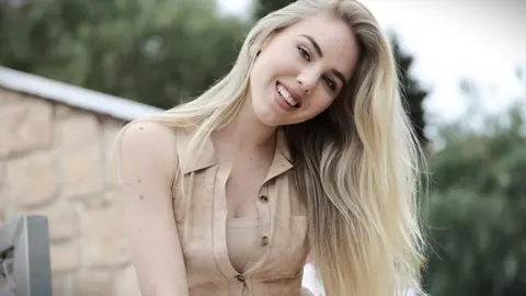 Portret mlade plavuše u bež odjeći koja se smije