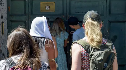 Grupa turista stoji u redu ispred velikih zelenih drvnih vrata
