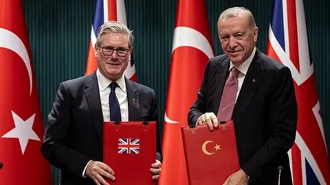 Keir Starmer i Recep Tayyip Erdoğan drže crvene mapه s zastavama država.