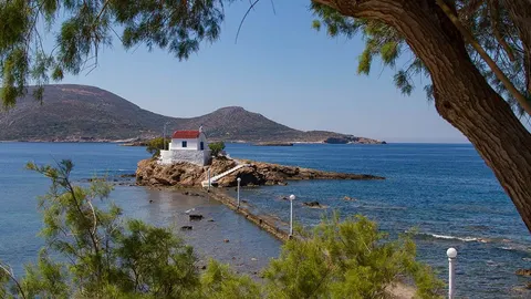Bijela grčka crkvica s crvenim krovom na stjenovitoj obali pored plavog mora
