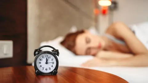 Crni alarmni sat na drvenom stolu s osobom koja spava u pozadini