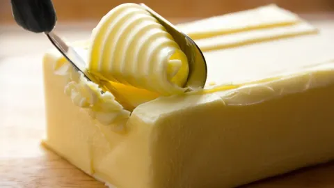 Krupni plan noža koji zakidaje komad žutog maslaca
