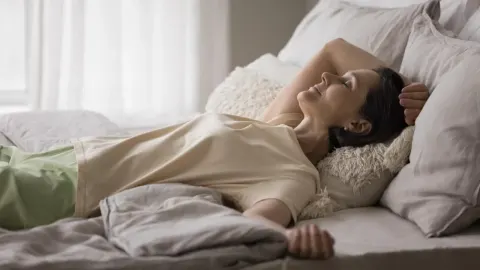 Žena srednjih godina mirno spava u krevetu na svijetlim jastucima.
