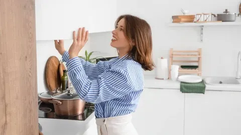 Žena u prugastoj košulji čisti gornje elemente u svijetloj kuhinji