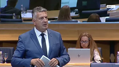 Muškarac u plavom odelu i crnoj kravati govori u parlamentarnoj sali
