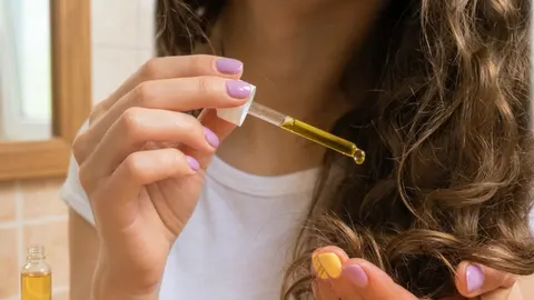 Žena nanosi prirodno ulje iz pipete na svoje kovrčave smeđe vlase