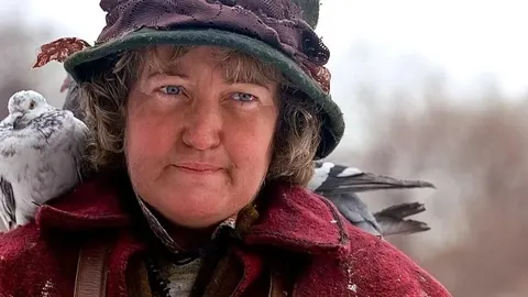Brenda Fricker u crvenom kaputu i šeširu s golubovima na ramenima