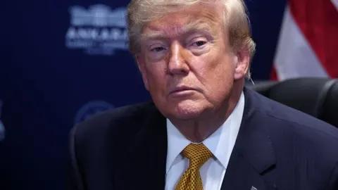 Portret Donalda Trumpa u tamnom odelu i žutoj kravati sa ozbiljnim izrazom lica