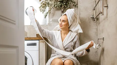 Žena u bijelom bademantilu s ručnikom na glavi u kupaonici