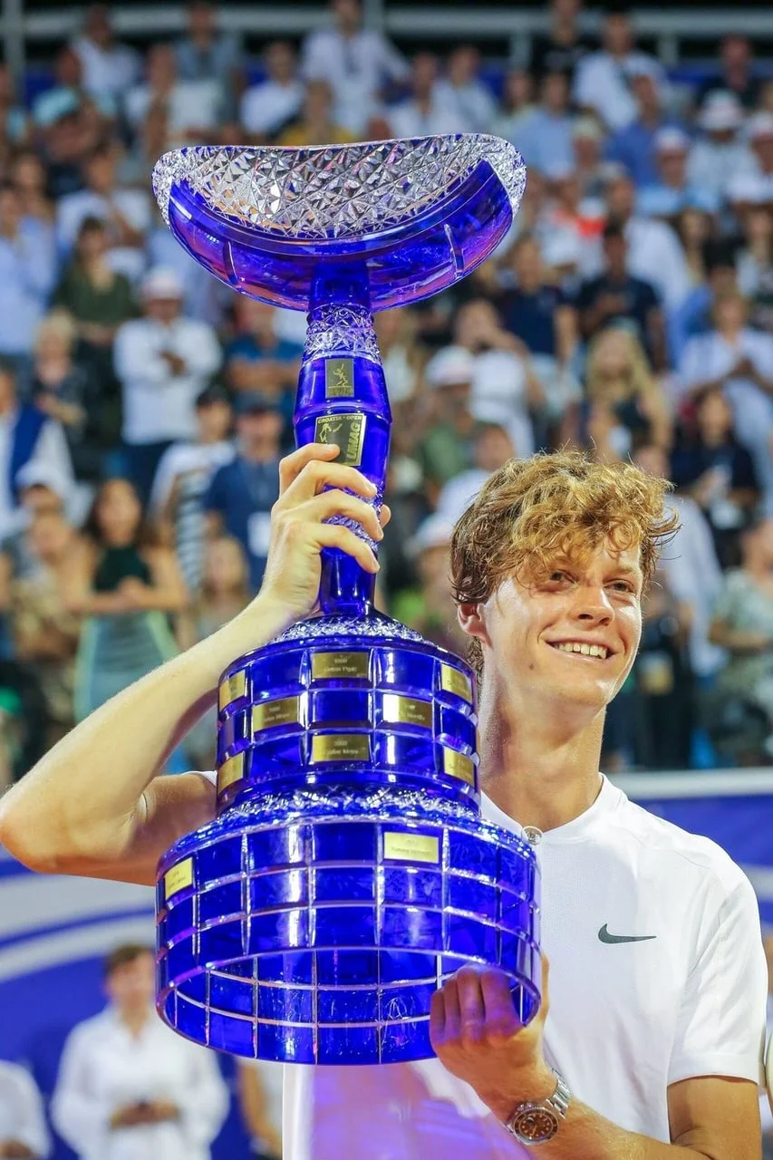 Tenisač Jannik Sinner smiješeći se i držeći veliki plavi kristalni trofej