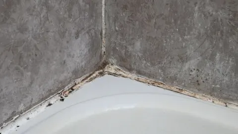 Crna buđ na silikonskom spoju između kade i sivi zidnih pločica