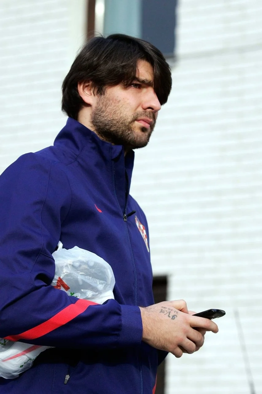 Vedran Ćorluka u plavoj reprezentativnoj jakni drži mobitel